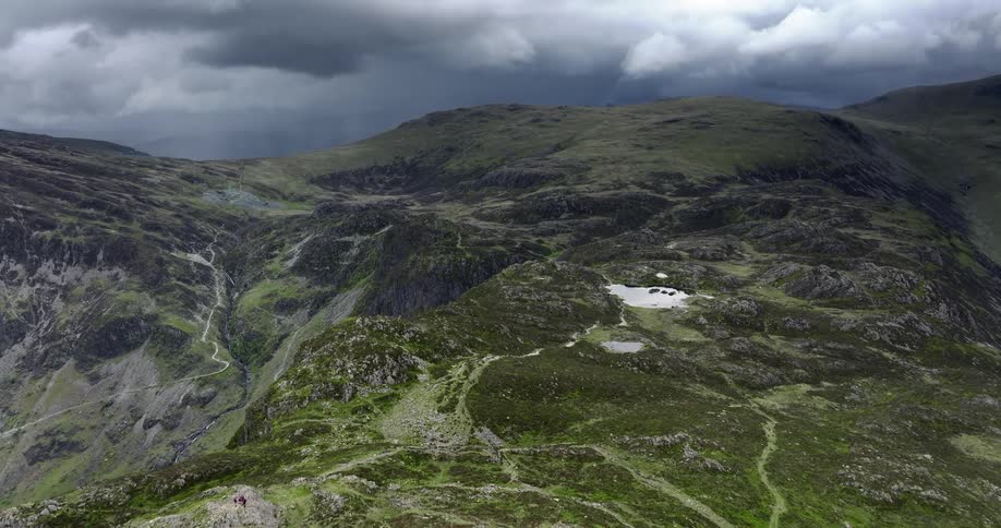 Grass grows on a rocky mountain ridge with a frozen lake and there are mountains on the horizon under a dark cloudy sky