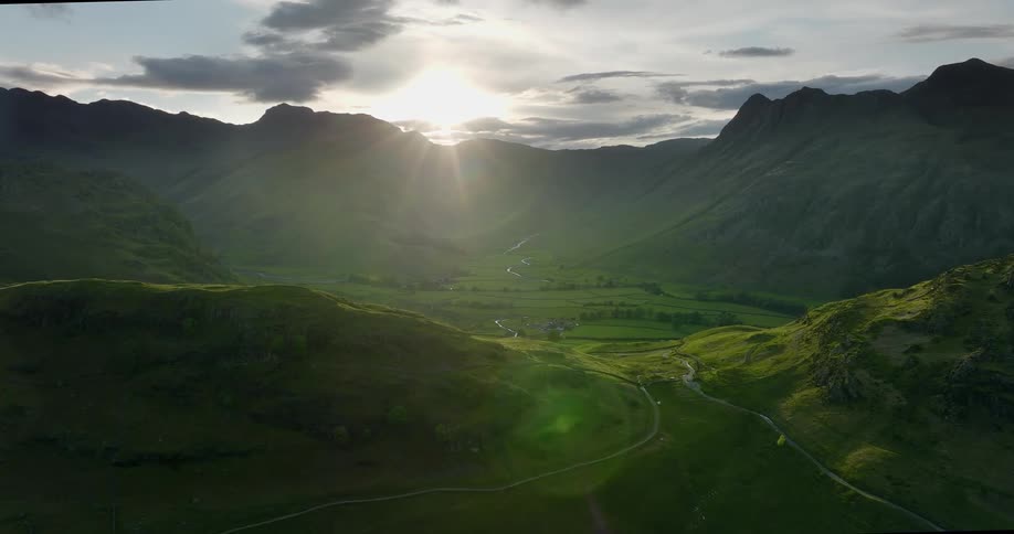 Road runs through the green fields surrounded by mountains on a sunny day