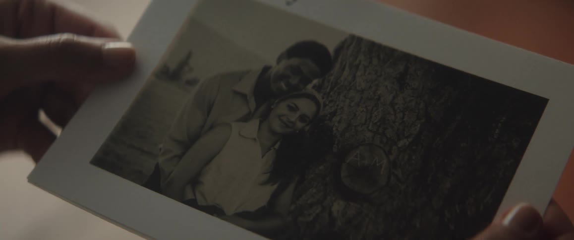 A woman holds a photo of a man and woman posing by a tree