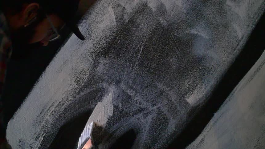 An artist paints a stroke of white paint onto a wall