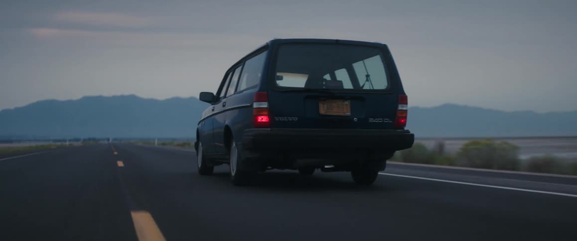 A volvo wagon travels on an empty rural road with the silhouette of hills on the horizon