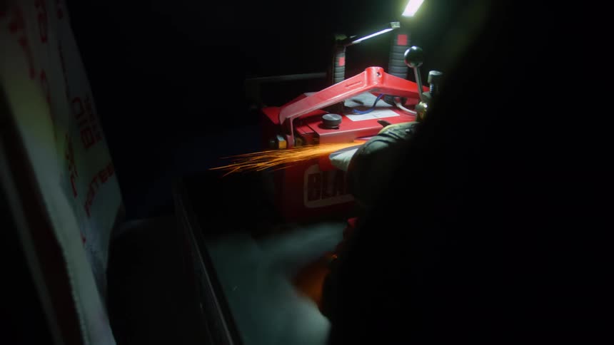 Close up of a power tool cutting a piece of machinery over a workbench inside a dimly lit room