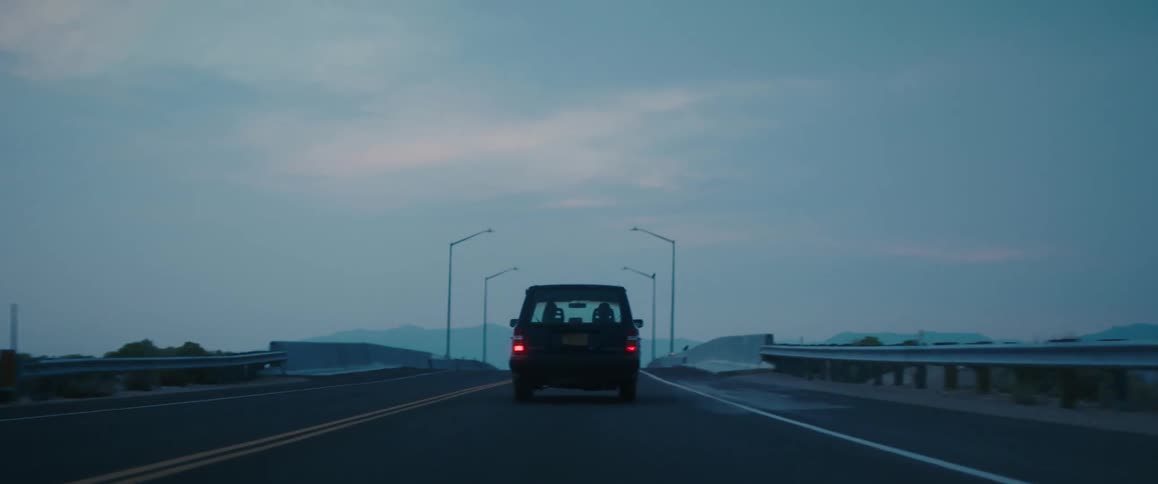 A flock of birds flies overhead as an old volvo suv begins to travel over a bridge