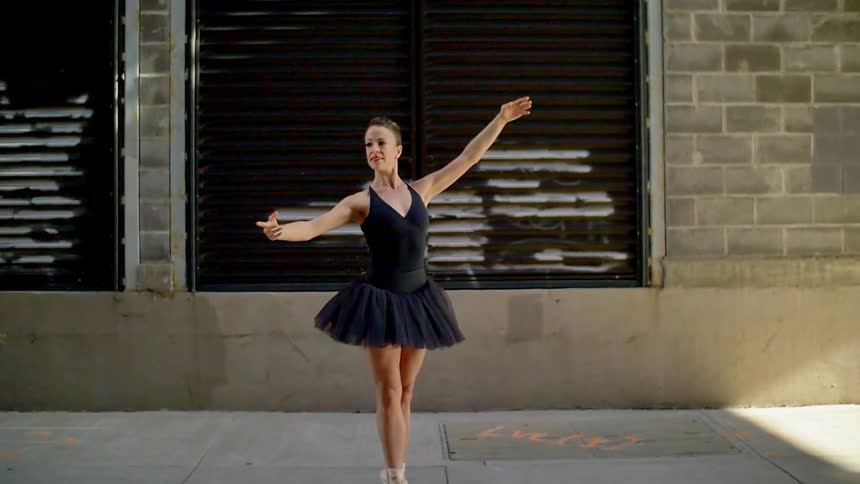 A woman is ballet dancing in front of a building