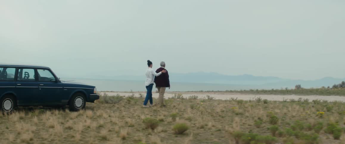 A woman helps guide a man as they walk through the brush toward the sand
