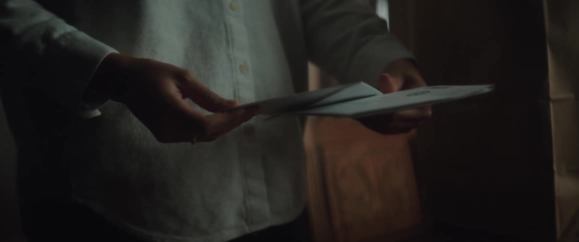 A woman puts a paper grocery bag down on the table and picks up the mail opening a card
