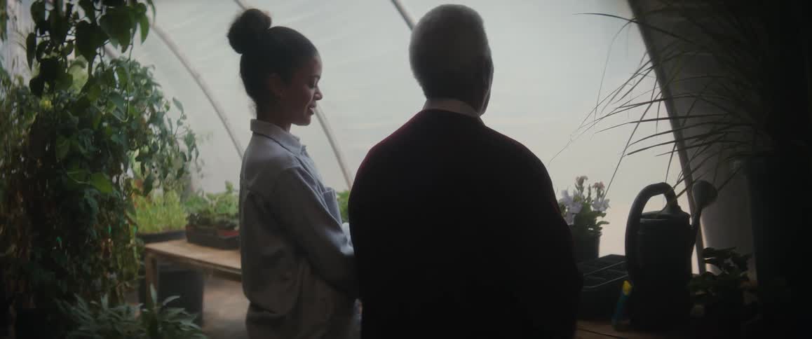 Two people stand talking at potting bench in large greenhouse