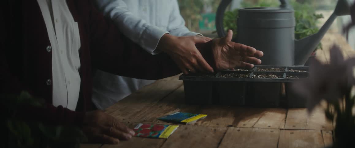 An old man is helping a woman plant seeds in a container