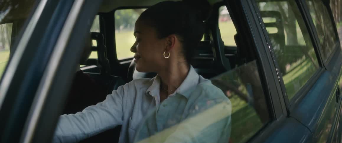 A young woman is driving an automobile and she looks over to her side and smiles