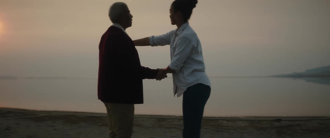 Daughter helps her blind father to skip rocks on the surface of the ocean from a beach at sunset
