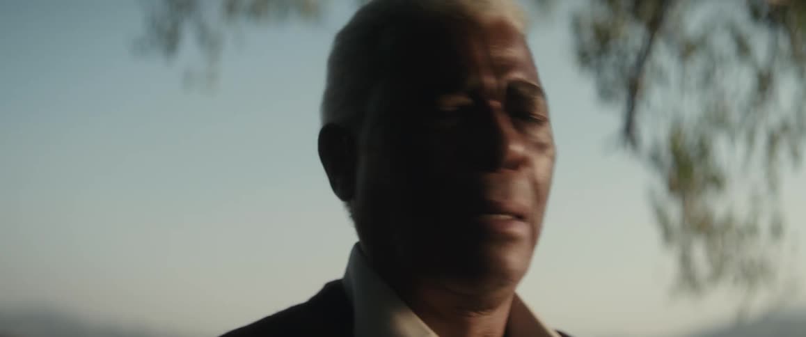 The sun shines on the face of an elderly black man as he stands outside with his eyes closed and appears to be very emotional