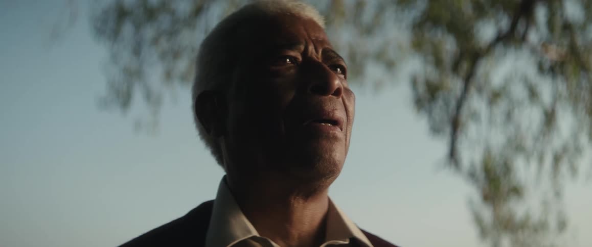 An old man standing outside near a tree overcome with emotion