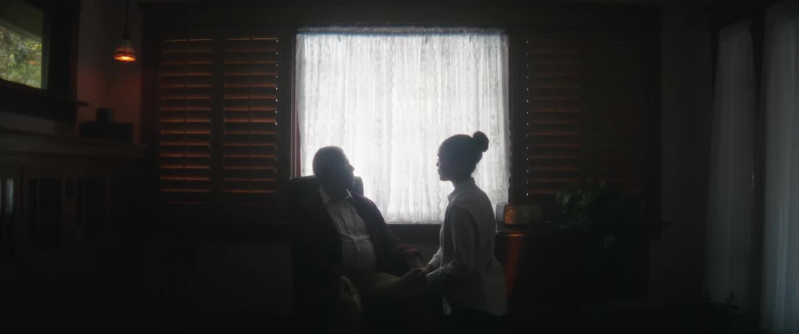 A woman carries a bag into a room then sits with a man and he caresses her face with his hand