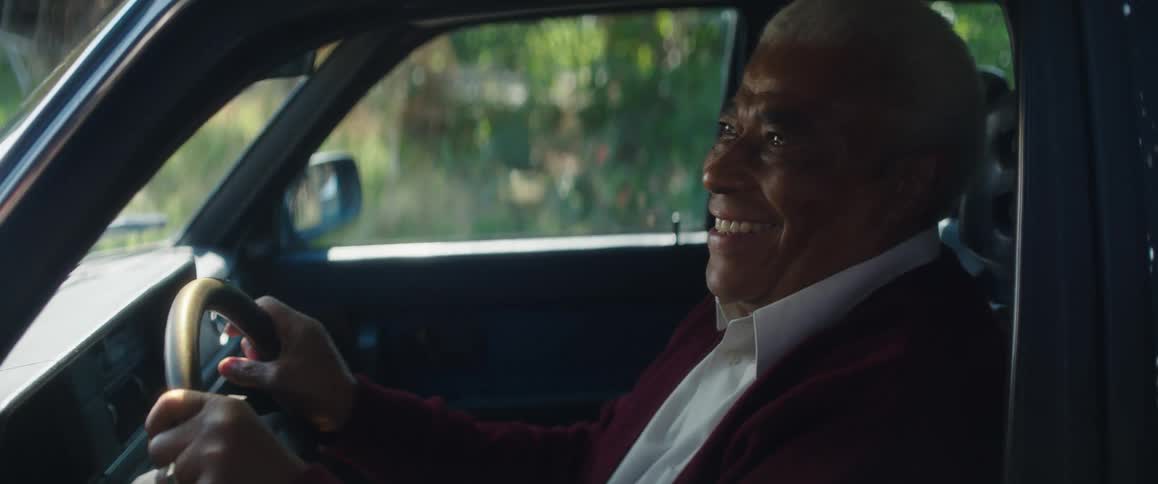 Elderly man laughs while holding the steering wheel of a parked car