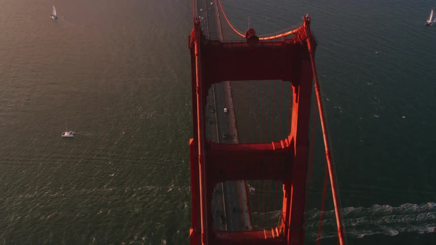 Traffic moves across a suspension bridge as a boats sail in the water below