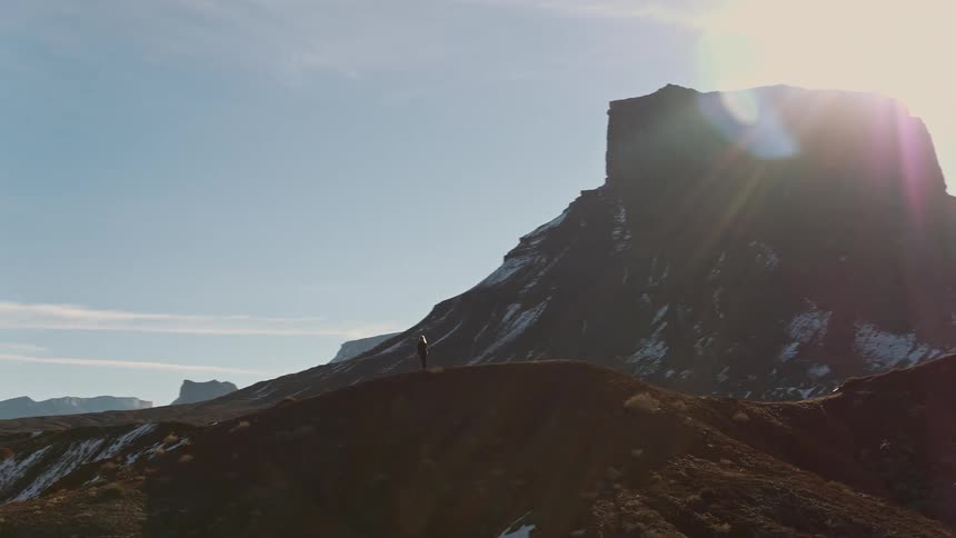 A person stands on a hill across from a tall mesa in a canyon