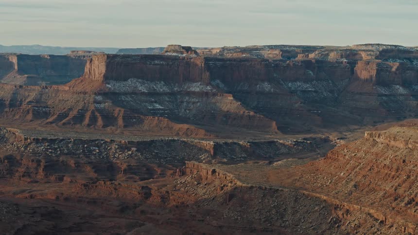 Plateau and mesas occupy canyon with misty mountains on the horizon under an overcast sky