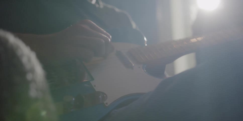 A man sitting back in a chair picking the strings of an electric guitar
