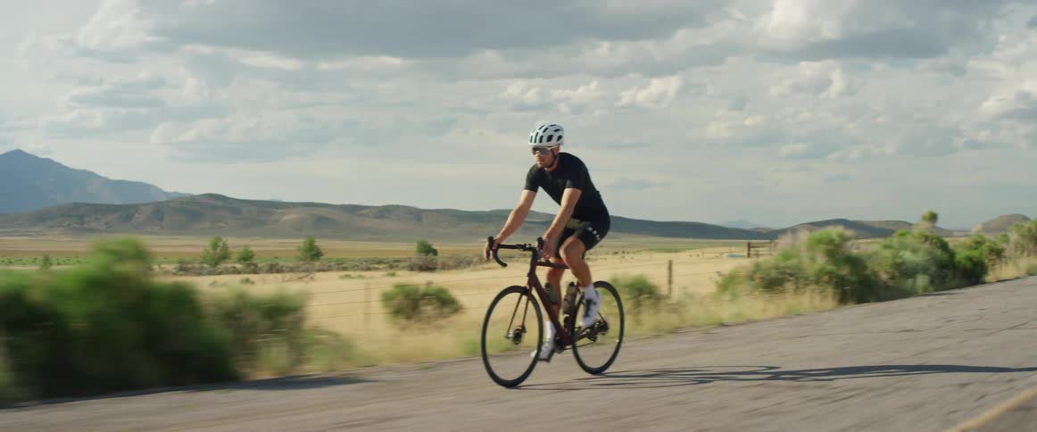 A man cycles on a road past farmland
