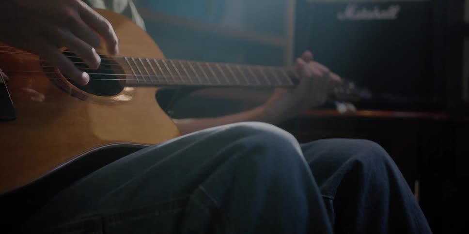 A man is sitting in a room playing an acoustic guitar