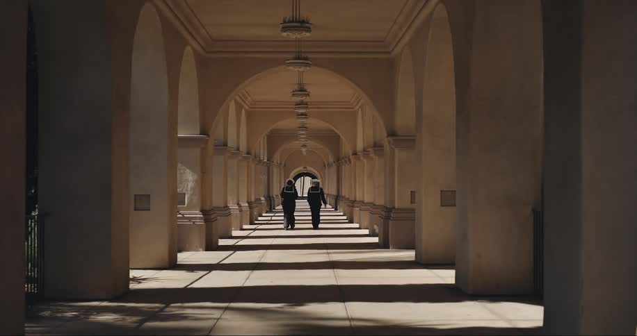 Two people in sailor uniforms walk down an arched hallway