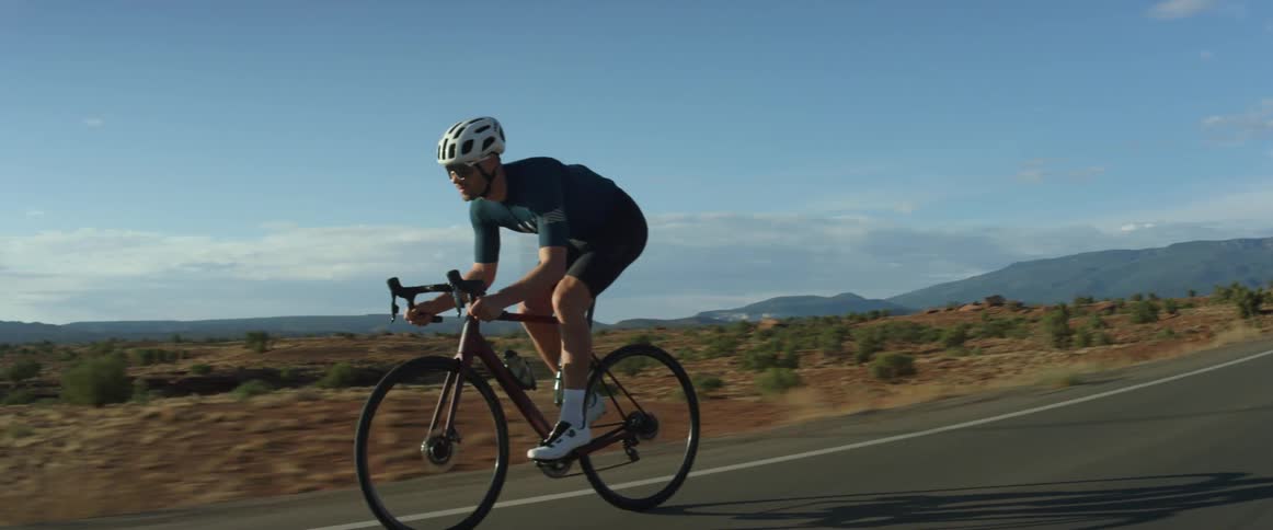 A man pedals his bike then coasts on an empty highway through the desert