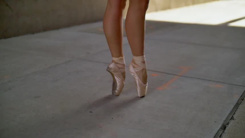 A woman dances on her tiptoes on a sidewalk