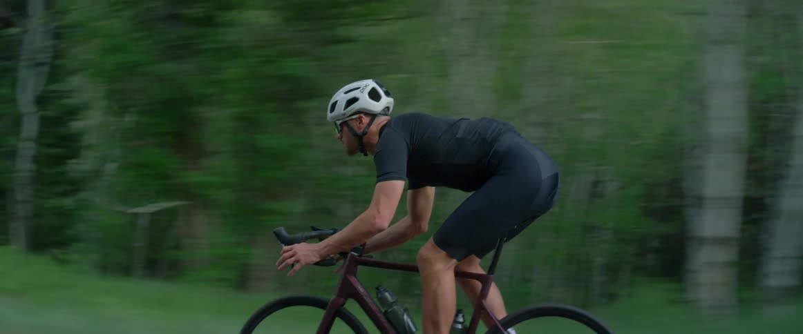 A man rides his bicycle past a forest