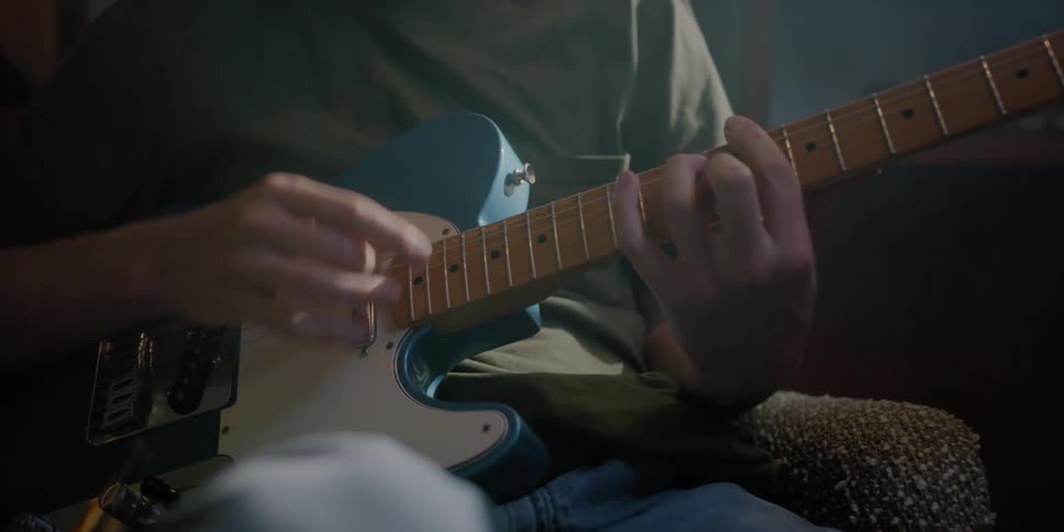 A young man playing guitar in a room during the day