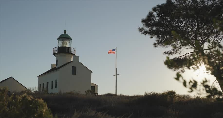 Wind blows american flag on flagpole near building with light beacon