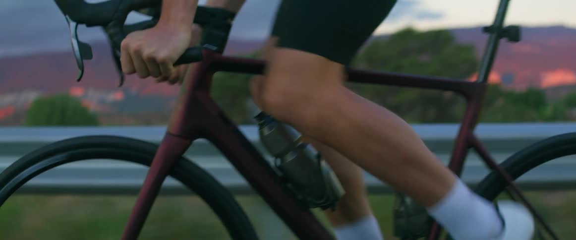 A man riding a bicycle is pedaling fast as he travels on a road near a guard rail