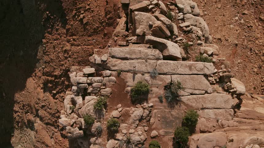 A mountain climber stands atop a rock formation atop a mountain in the desert
