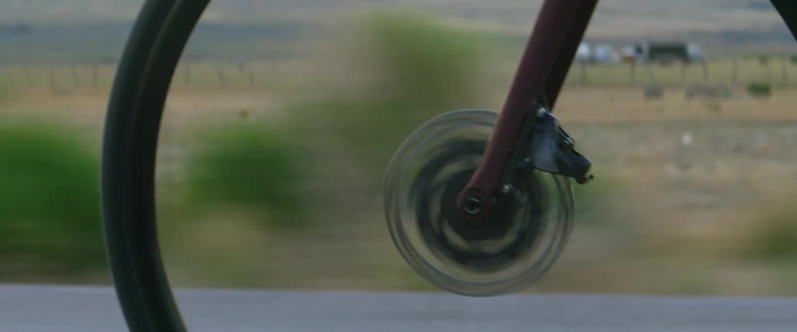 Cyclist pedals along highway passing fenced pastures with mountains in the distance