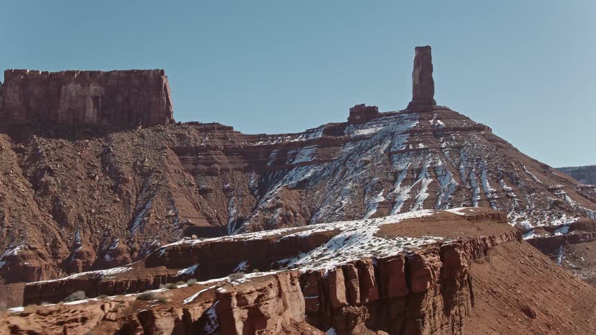 Light snow covers parts of badland mesa and rock formations under a clear blue sky