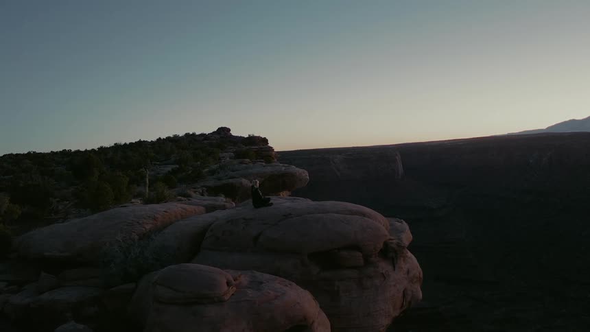 A woman sits atop a cliff at sunrise in the southwestern united states