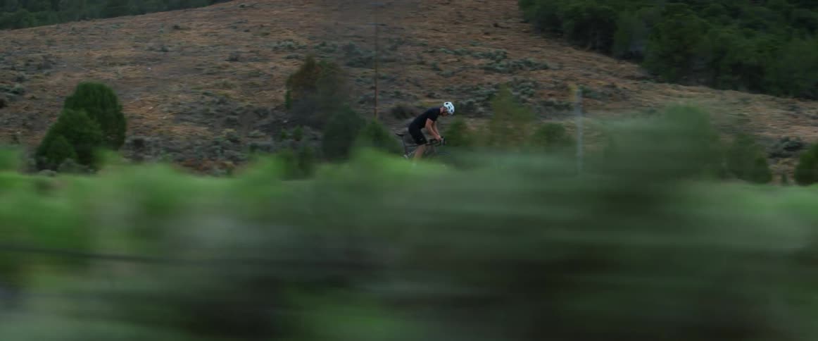 A man lifts up off the seat to pedal his bike on a rural road