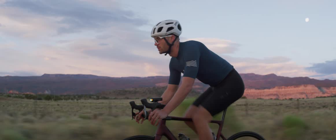 Male cyclists pedals rapidly while cycling along road with mountains in the background