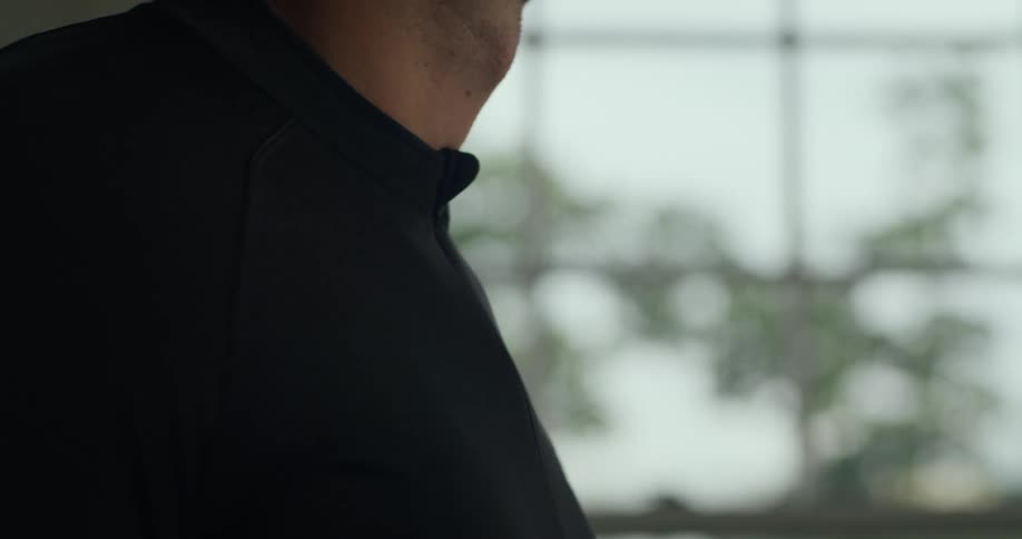 A man zips up his shirt before walking out of frame