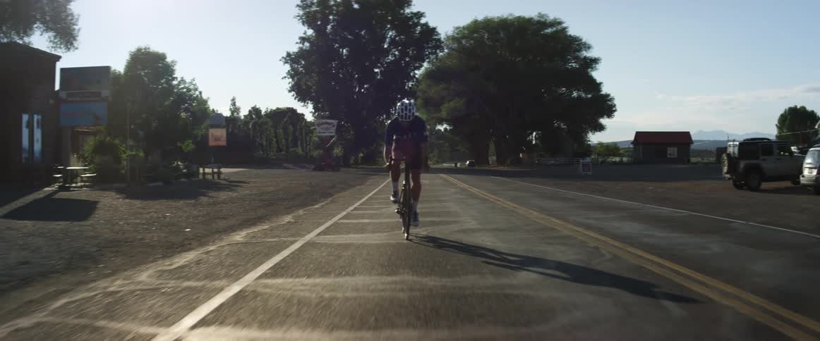 Cyclist rides along street past parking lot and buildings with mountains on the distant horizon