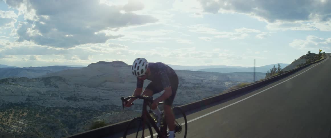 Cyclists rides along side of highway overlooking wide valley on a cloudy day