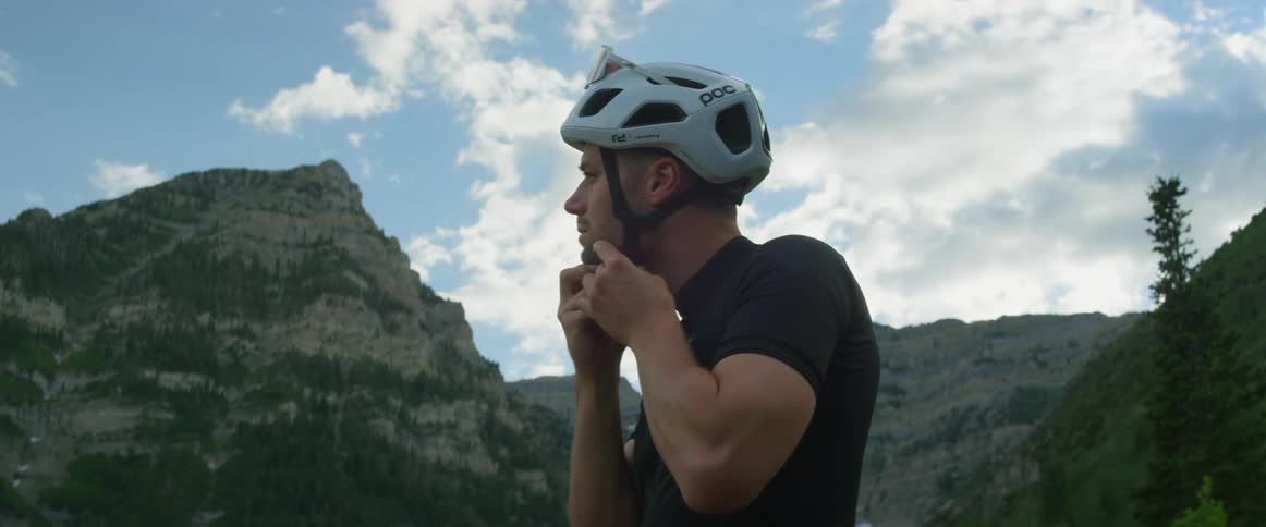 A man puts on a biking helmet and a pair of sunglasses while preparing to cycle in the mountains