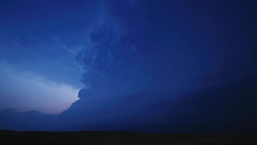 A massive super cell thunderstorm rises high into the atmosphere as an intense bolt of lightning flashes in the massive storm with blue and purple light