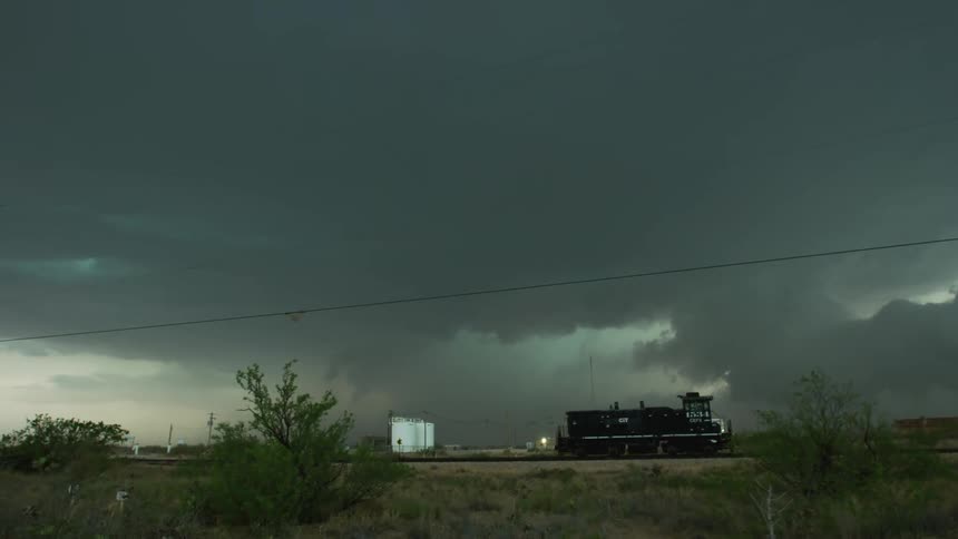 A massive bolt of high intensity lightning strikes extremely close to camera with a train locomotive and severe thunderstorm in the background