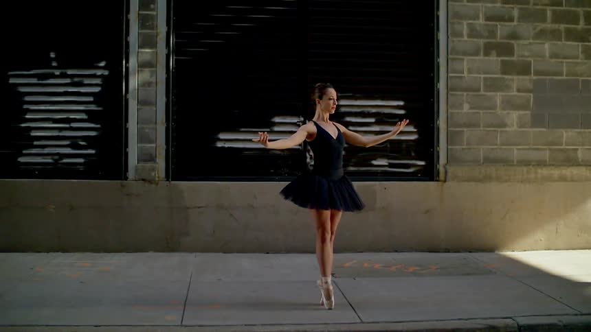 A woman ballet dances on the sidewalk