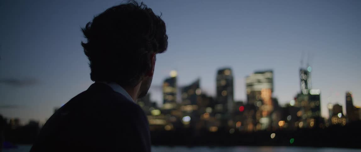 A man is outside looking at buildings and skyscrapers lit up in the big city skyline