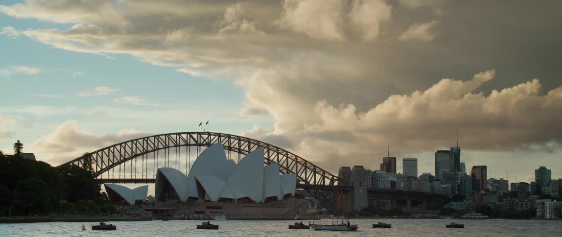 Boats are floating in the ocean near an opera house in a large city