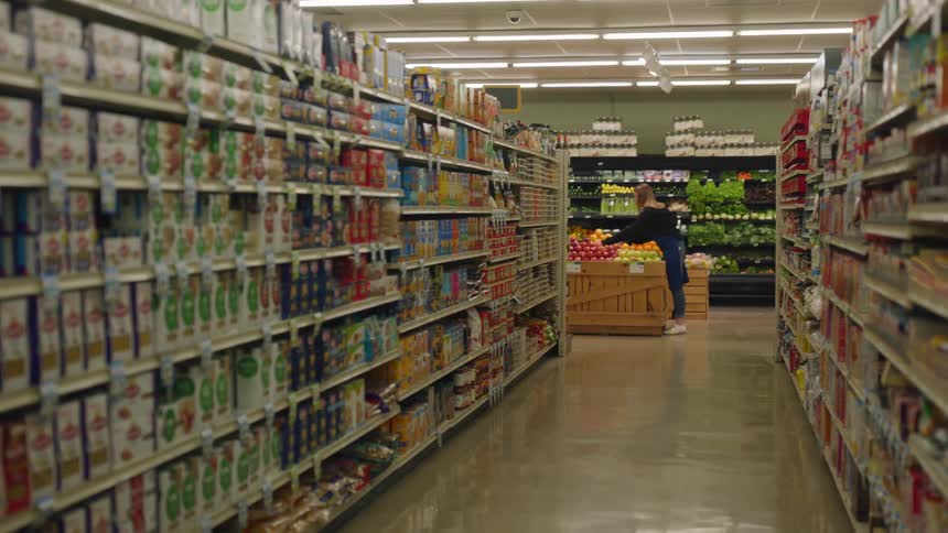 A female grocery store clerk arranges fruit at the end of a long aisle