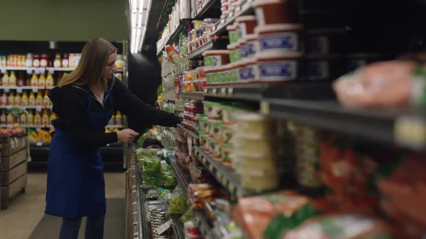 A female grocery store worker is arranging products on a shelf