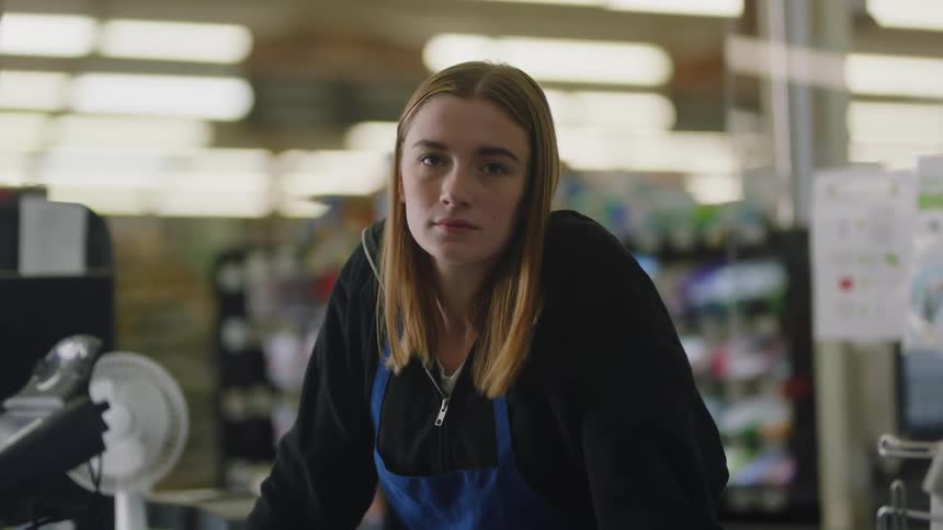 Close up of a young blonde woman looking at the camera inside a small store