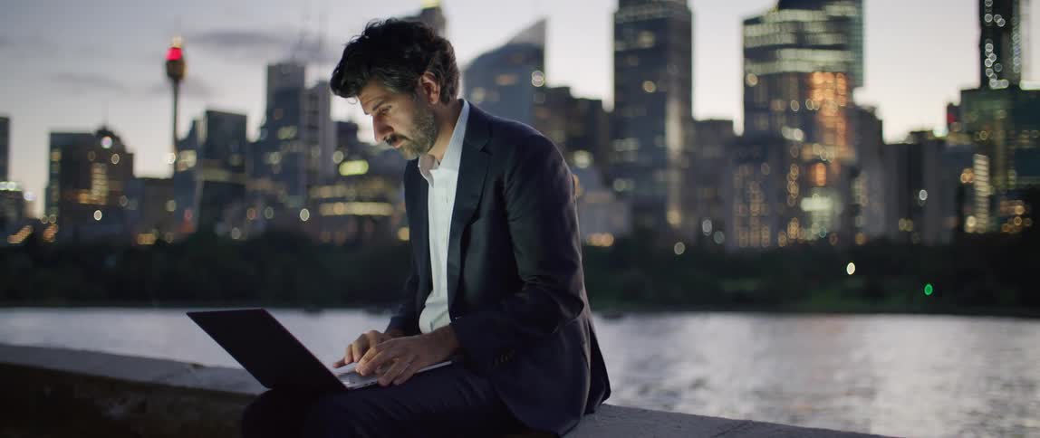 A man is typing on his laptop by the city